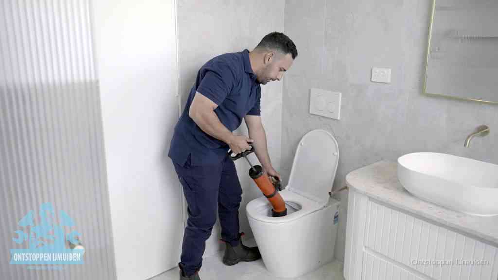 Een monteur buigt over een wandcloset en duwt met de hand een persluchtontstopper in de toiletpot om de verstopping handmatig los te maken in IJmuiden