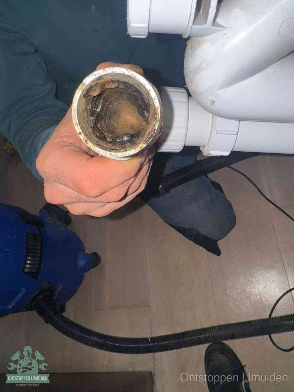Een hand houdt een losgekoppeld PVC-afvoerbuisstuk vast dat van binnen volledig is dichtgeslibd met vet, vuil en aanslag, de meest voorkomende oorzaak van een verstopte afvoer in IJmuiden