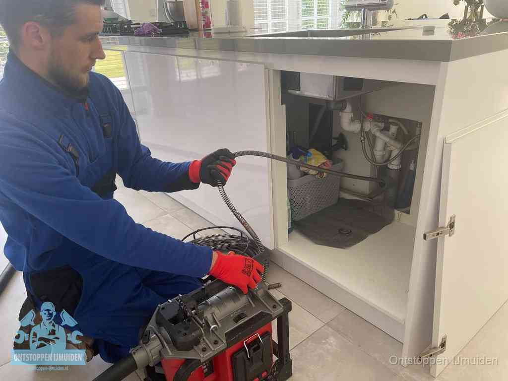 Monteur voert een ontstoppingsveer in de afvoer onder de keuken in IJmuiden