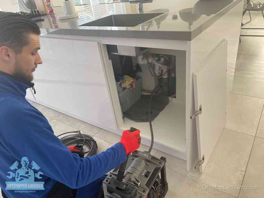 Monteur ontstopt met een veermachine een verstopte afvoer onder de gootsteen in IJmuiden