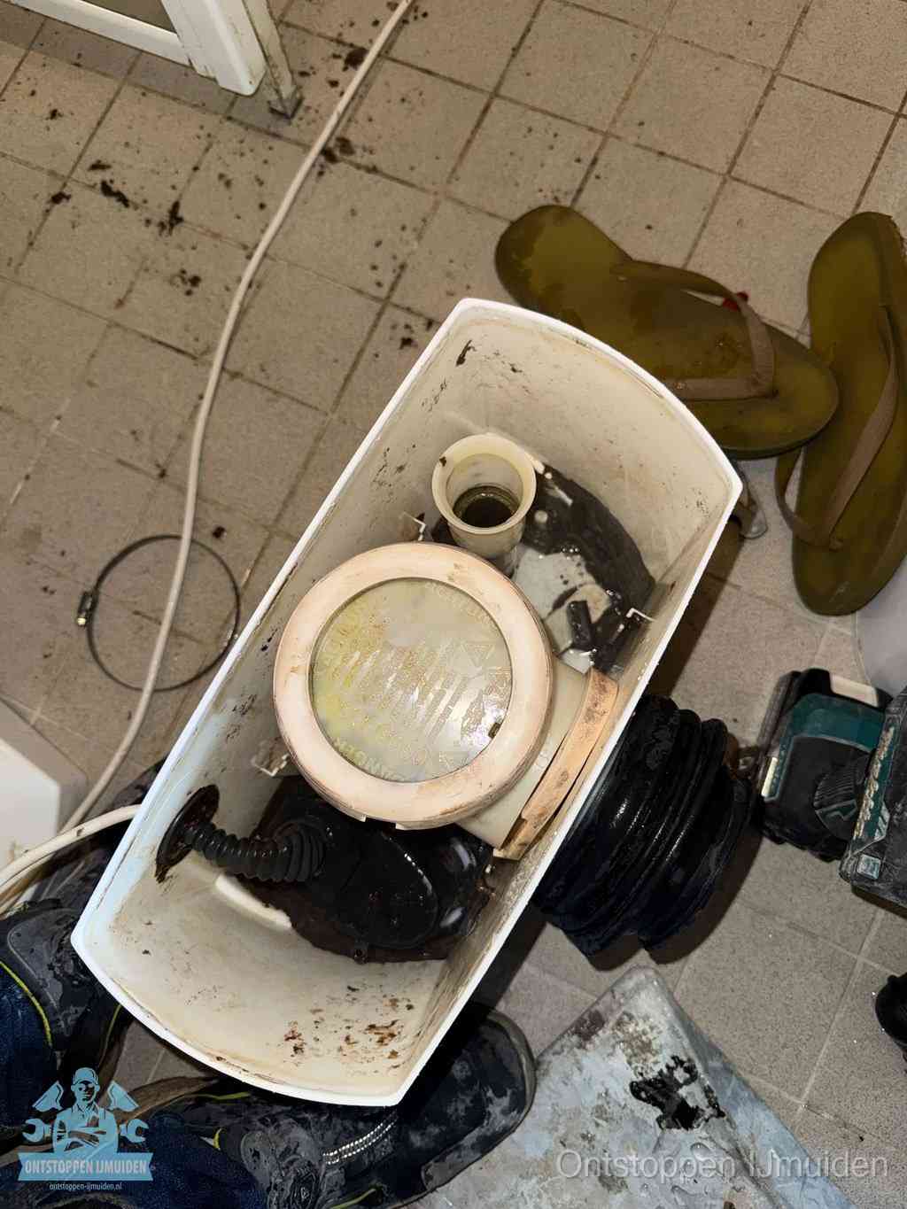 Een gedemonteerde toiletpot op de vloer met ontstoppingsveer en gereedschap ernaast, het verwijderen van een vastzittend voorwerp uit de wc in IJmuiden